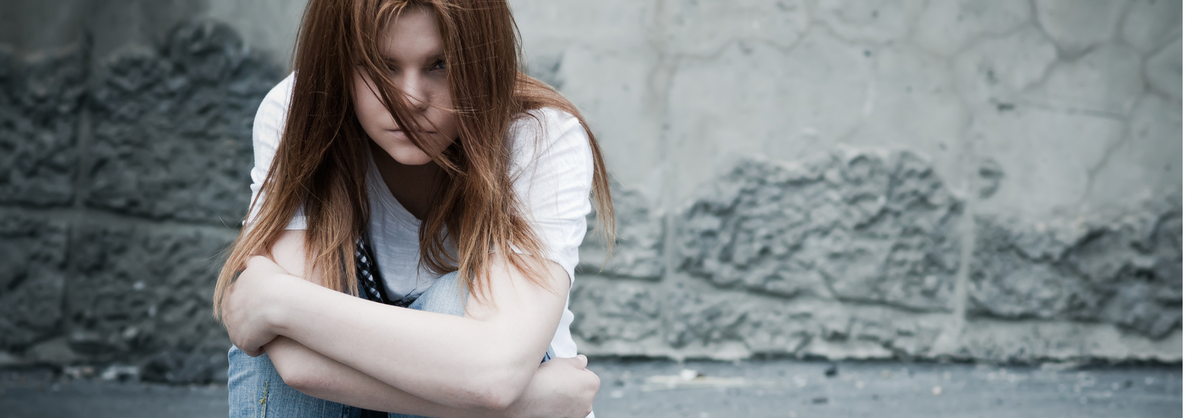 A sad teen girl with long hair sits alone on the sidewalk